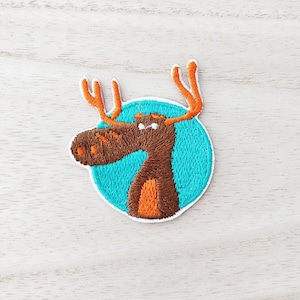 May include: Embroidered iron-on patch of a brown moose with orange antlers, looking to the left, on a turquoise blue circle.