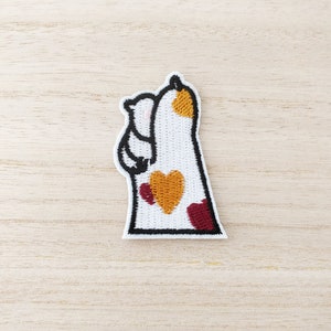 May include: White embroidered iron-on patch of a cat with red and yellow hearts. The cat is standing on its hind legs with its front paws raised.