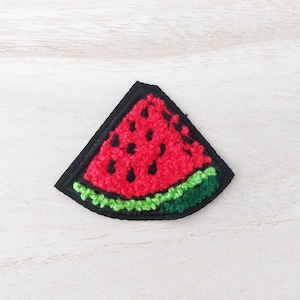 May include: A red watermelon slice with black seeds and a green rind, embroidered on a black felt patch.