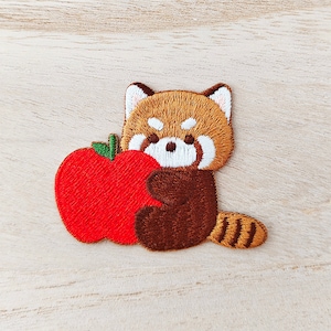 Peut inclure: Écusson brodé représentant un panda roux de dessin animé tenant une pomme rouge. L'écusson est de couleur marron, beige, blanc et rouge. Le panda roux a une queue rayée et tient la pomme. Idéal pour les vêtements ou accessoires.