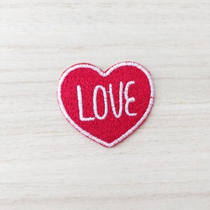 May include: Red felt heart-shaped patch with white embroidered lettering that says "LOVE".