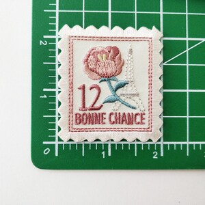 May include: A white embroidered patch with a pink flower, a blue Eiffel Tower, and the text "12 BONNIE CHANCE".