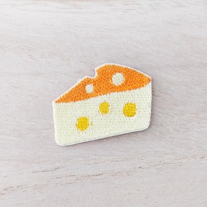 May include: An embroidered patch of a wedge of cheese with holes, in yellow and orange.