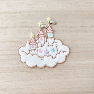 May include: A white felt patch with an embroidered image of a pink castle on a cloud. The castle has yellow stars and flags. The cloud has a brown outline.
