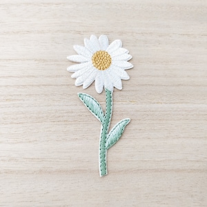 Peut inclure: Fleur de marguerite blanche brodée avec un centre jaune et une tige et des feuilles vertes.