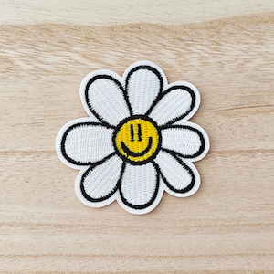 Peut inclure: Écusson en forme de marguerite blanche avec un centre jaune représentant un smiley et un contour noir. La marguerite a des pétales blancs et un visage jaune souriant. Ce patch peut être thermocollé ou cousu.