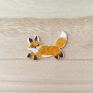 Peut inclure: Écusson brodé d'un renard courant. Le renard a une fourrure orange avec une poitrine et une pointe de queue blanches. Les oreilles et les pieds du renard sont brun foncé. L'écusson est bordé de blanc.