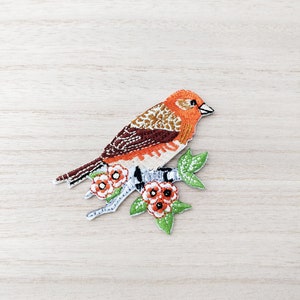 May include: Embroidered iron-on patch of an orange and brown bird perched on a branch with green leaves and orange flowers.