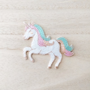 Peut inclure: Patch brodé blanc en forme de licorne avec une crinière et une queue rose et turquoise.