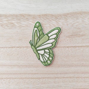 May include: Green embroidered butterfly patch with white accents. The butterfly is facing right and has its wings spread out.