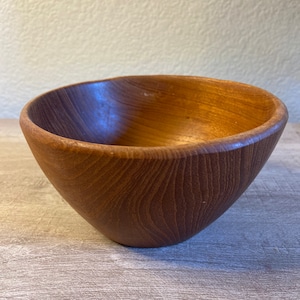 May include: A wooden bowl with a natural brown finish. The bowl is round and has a smooth, slightly curved surface.