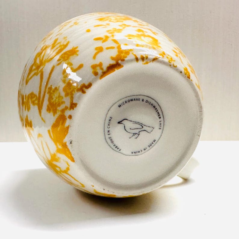May include: A white ceramic mug with a black handle and the text "But First, Coffee" in a handwritten style. The mug is on a white surface. The mug is 10 cm tall.