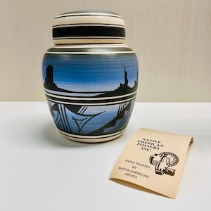 May include: A blue and white ceramic jar with a black and white geometric design. The jar has a lid and is hand-painted by Native American artists. The label reads "Native American Pottery Inc."