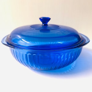 May include: A cobalt blue glass casserole dish with a matching lid. The dish has a ribbed design on the exterior and a small handle on the lid. The dish is likely vintage and suitable for serving or storage.