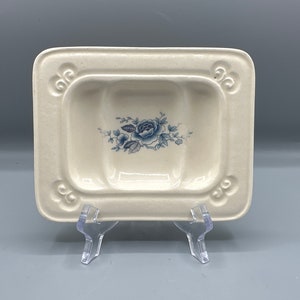 May include: A white ceramic dish with three sections and a blue floral design. The dish has a decorative border with a scalloped edge.