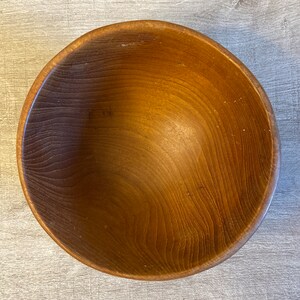May include: A large, wooden bowl with a natural brown finish. The bowl is made of wood with a smooth, polished surface.