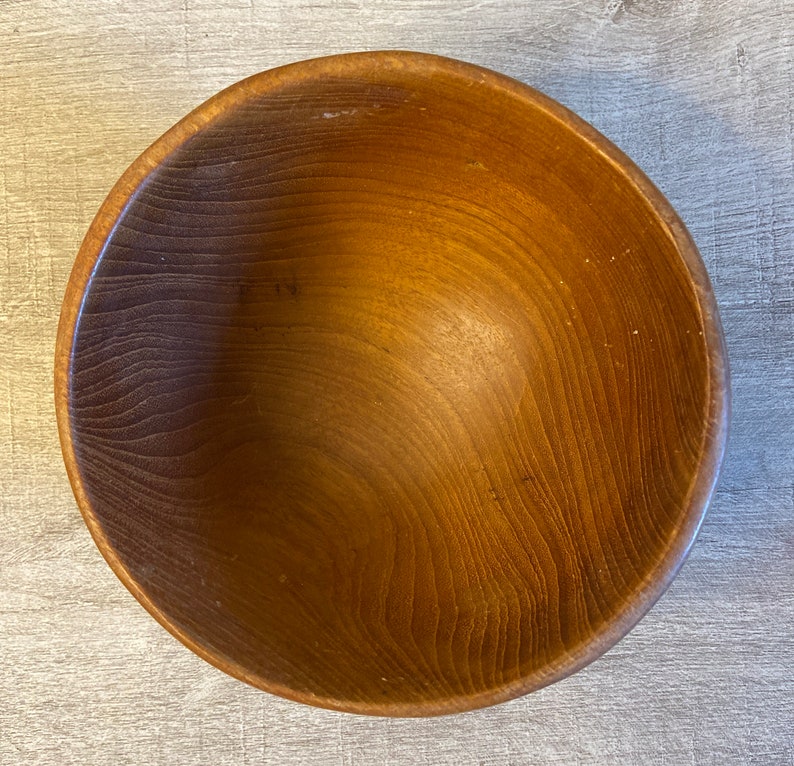 May include: A large, wooden bowl with a natural brown finish. The bowl is made of wood with a smooth, polished surface.