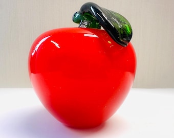 May include: A vibrant red glass apple sculpture with a glossy finish. The apple features a dark green stem and leaf, adding contrast to the bright red body. This decorative piece is ideal for home decor.