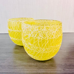May include: Two yellow glass bowls with a white lace pattern. The bowls are round and have a slightly flared lip.