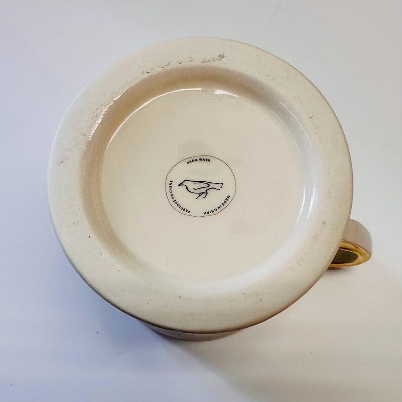 Puede incluir: La parte inferior de una taza de cer&aacute;mica blanca con un logotipo de p&aacute;jaro negro y el texto "Made in China, Lavar a mano, Fabriquer en Chine".