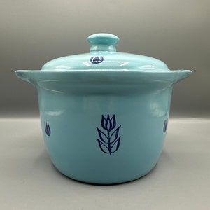 May include: A light blue ceramic pot with a lid, featuring a blue tulip design. The pot has a rounded shape and two handles.