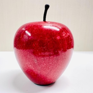 May include: A red, shiny, marble apple with a black stem.