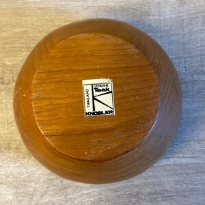 May include: A wooden bowl made of genuine teak wood from Thailand. The bowl has a label that reads "Genuine Teak" and "Knobler".