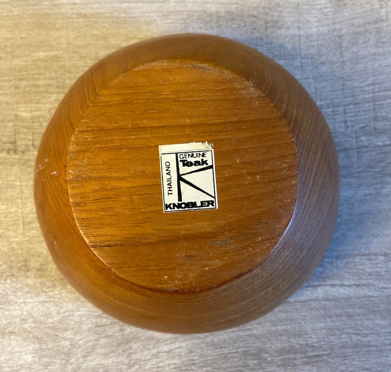 May include: A wooden bowl made of genuine teak wood from Thailand. The bowl has a label that reads "Genuine Teak" and "Knobler".
