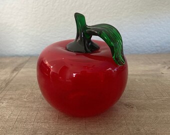 May include: A red glass apple with a green glass stem and leaf. The apple is shiny and has a smooth surface.