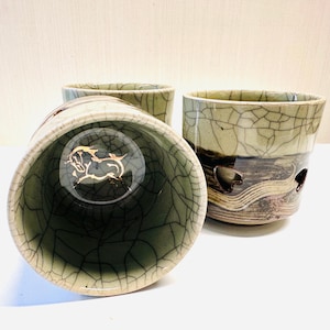 May include: Three ceramic cups with a crackle glaze finish. The cups are primarily olive green with brown and tan accents. One cup has a gold horse design inside. The cups have a unique, handcrafted appearance.
