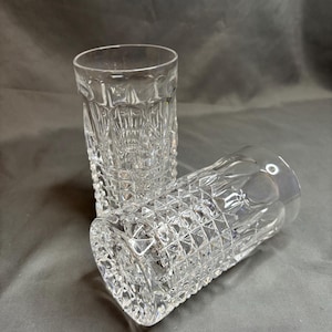 May include: Two clear, cut-glass tumblers with a diamond pattern. One tumbler is upright, while the other is lying on its side. The glasses are made of clear glass and have a textured surface.
