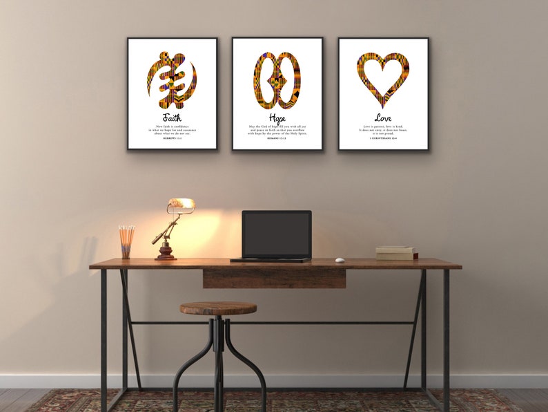 May include: Three framed prints with African Adinkra symbols and inspirational quotes. The prints are hung on a beige wall above a wooden desk with a lamp and a laptop. The quotes are "Faith", "Hope", and "Love".