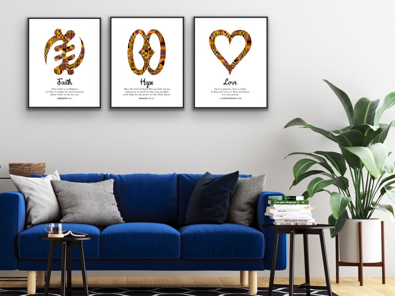 May include: Three framed prints with African Adinkra symbols and inspirational quotes. The prints feature the symbols for faith, hope, and love, each with a corresponding Bible verse. The prints are displayed on a white wall above a blue sofa.