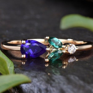 Op de afbeelding: Een gouden ring met een peer-vormige paarse edelsteen en drie peer-vormige groene edelstenen.