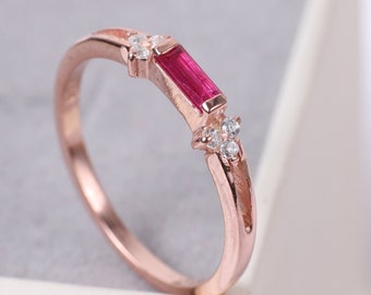 May include: A rose gold ring with a rectangular red gemstone and small clear gemstones.