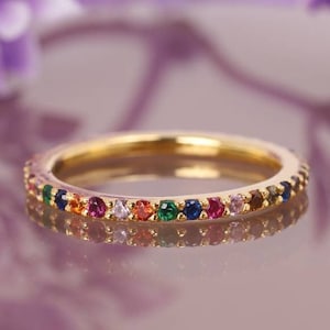 May include: A gold band ring with a rainbow of small gemstones set around the band.