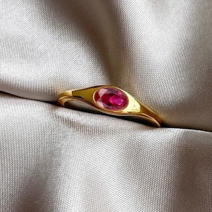 Op de afbeelding: Een gouden ring met een rode ovale edelsteen in het midden.