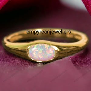 Op de afbeelding: Een gouden ring met een witte opaal edelsteen. De ring is gezet in een eenvoudige, ovale band.