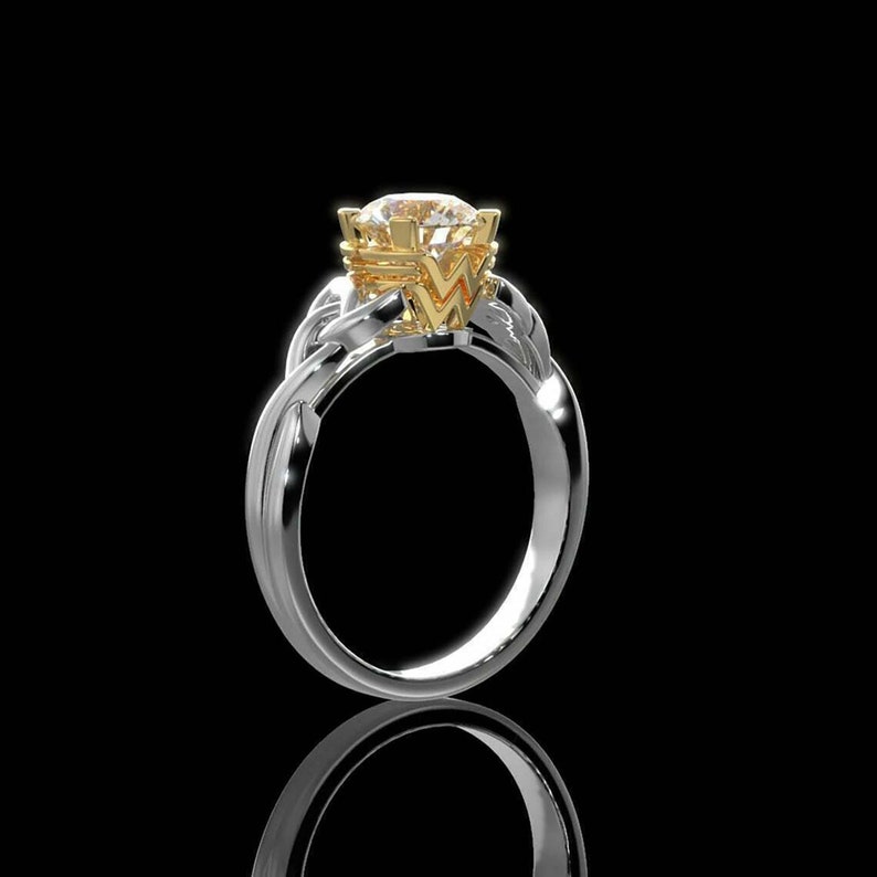 Op de afbeelding: Een zilveren ring met een gouden zetting en een grote, ronde, heldere edelsteen. De ring heeft een gedraaid bandontwerp en staat tegen een zwarte achtergrond.