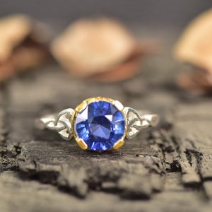 Op de afbeelding: Een zilveren ring met een grote, ronde, diepblauwe edelsteen gezet in een gouden bezel. De band van de ring heeft aan weerszijden van de edelsteen een Keltisch knoopontwerp.