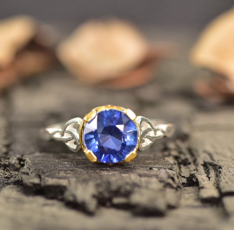 Op de afbeelding: Een zilveren ring met een grote, ronde, diepblauwe edelsteen gezet in een gouden bezel. De band van de ring heeft aan weerszijden van de edelsteen een Keltisch knoopontwerp.