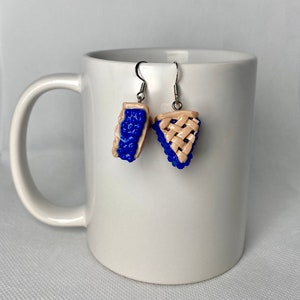 May include: A pair of dangle earrings featuring a blueberry pie design. The earrings are made of polymer clay and have a silver tone finish.