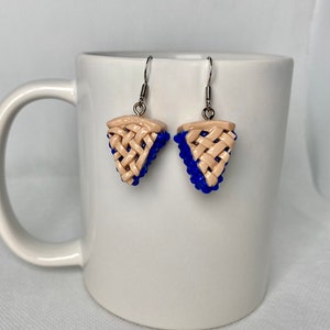 May include: A pair of dangle earrings featuring a blue and beige pie slice design. The earrings are made of polymer clay and have silver hooks.