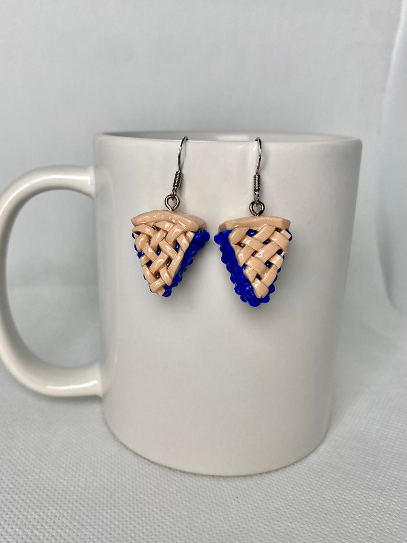 May include: A pair of dangle earrings featuring a blue and beige pie slice design. The earrings are made of polymer clay and have silver hooks.