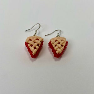 May include: A pair of dangle earrings featuring a red and beige pie crust design. The earrings are made of polymer clay and have silver hooks.