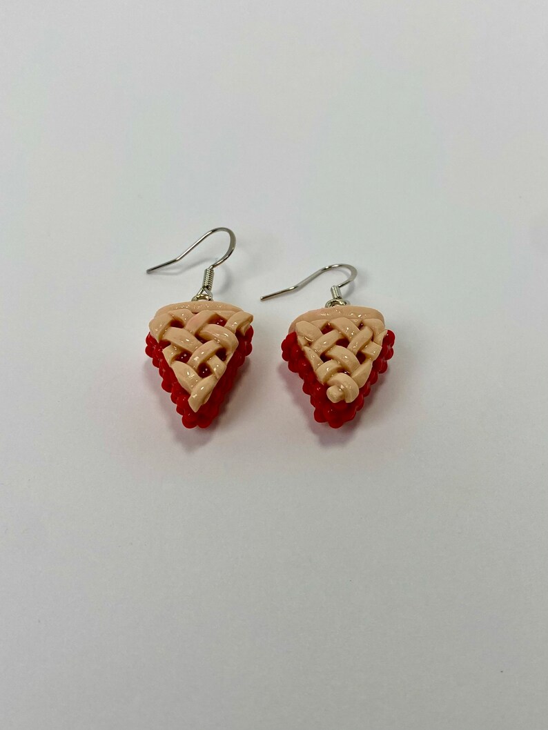 May include: A pair of dangle earrings featuring a red and beige pie crust design. The earrings are made of polymer clay and have silver hooks.