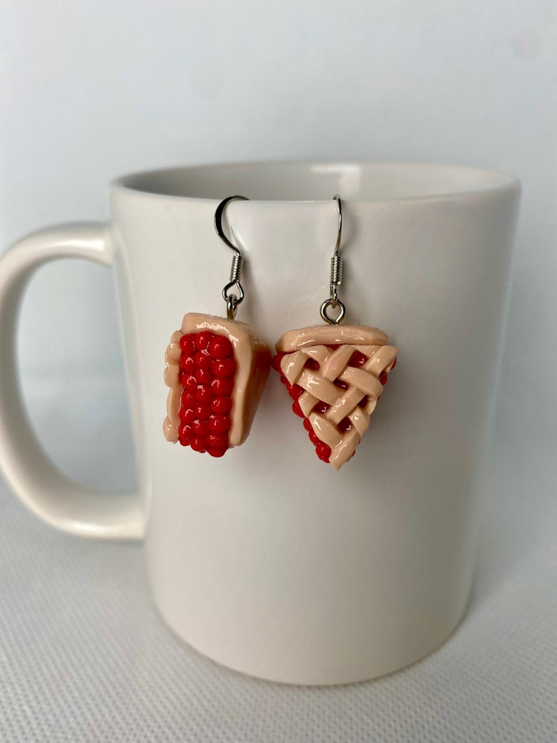 May include: A pair of dangle earrings featuring a red and pink pie slice design. The earrings are made of polymer clay and have silver hooks.
