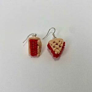 May include: A pair of dangle earrings featuring a red and beige pie design. The earrings are made of polymer clay and have silver hooks.