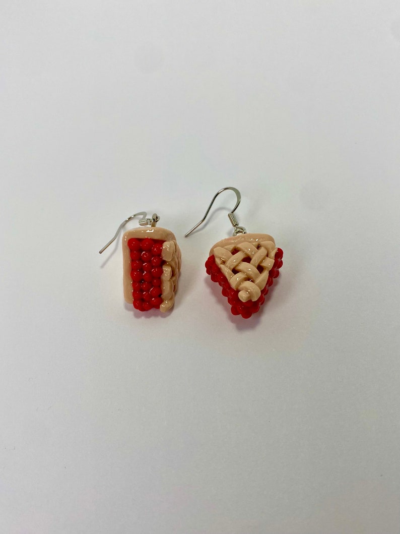 May include: A pair of dangle earrings featuring a red and beige pie design. The earrings are made of polymer clay and have silver hooks.