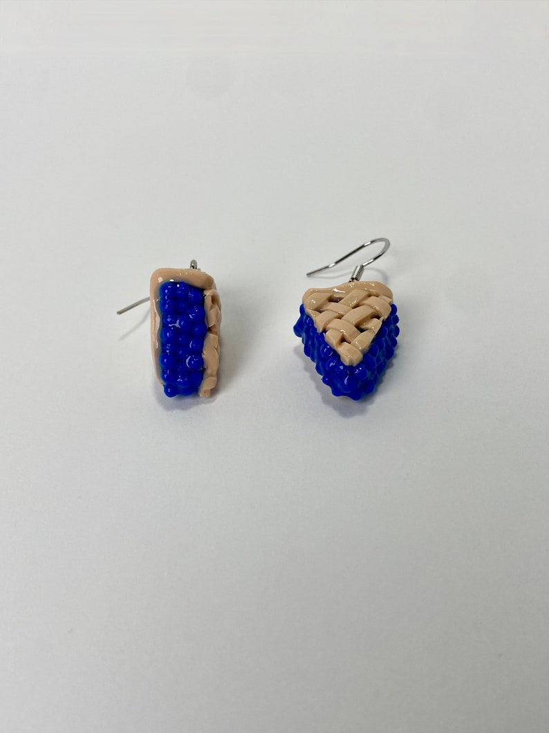 May include: A pair of blue and beige dangle earrings shaped like blueberry pie slices.